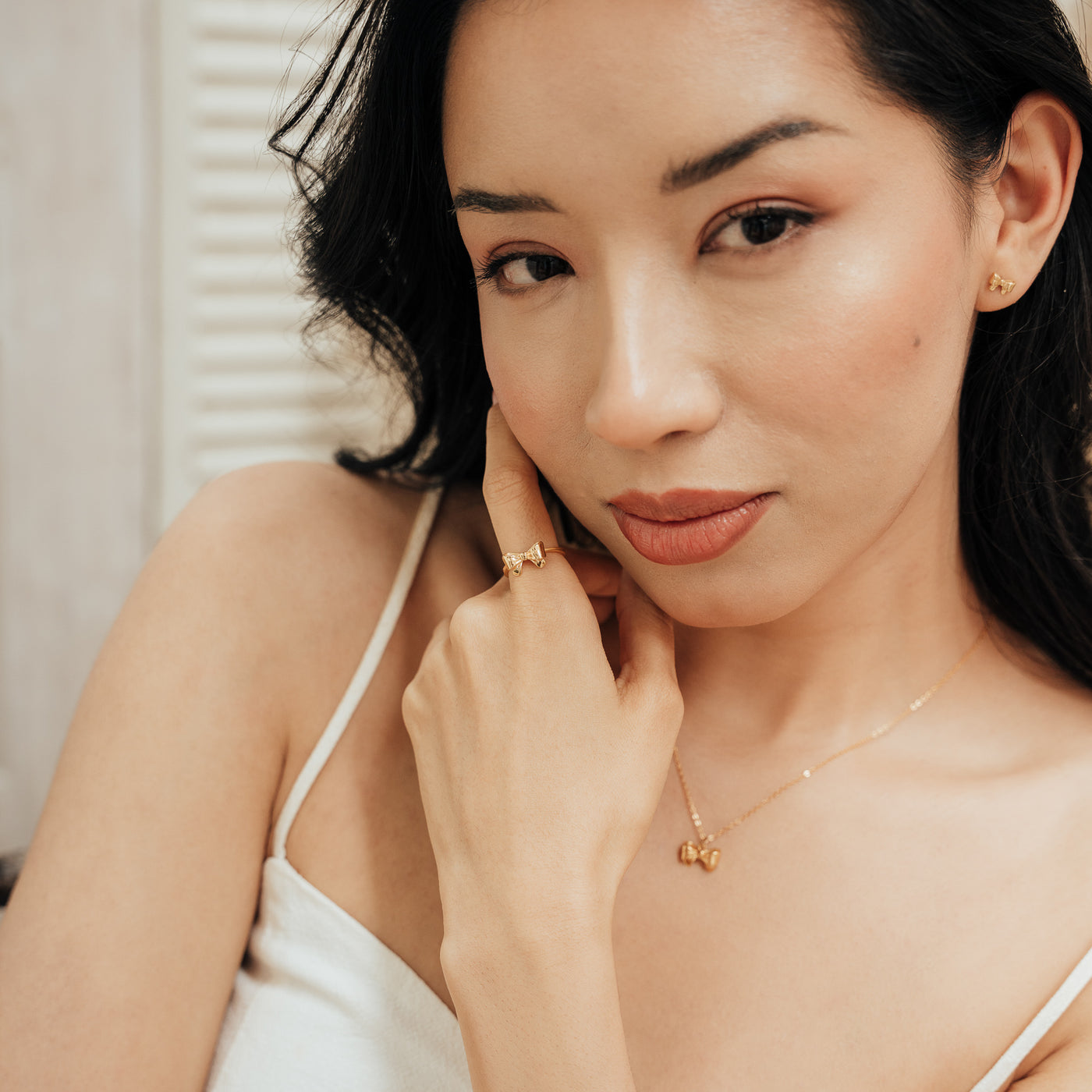 Woman with her hand near her face, wearing a Ribbon Bow Necklace and matching Ribbon Bow Ring.