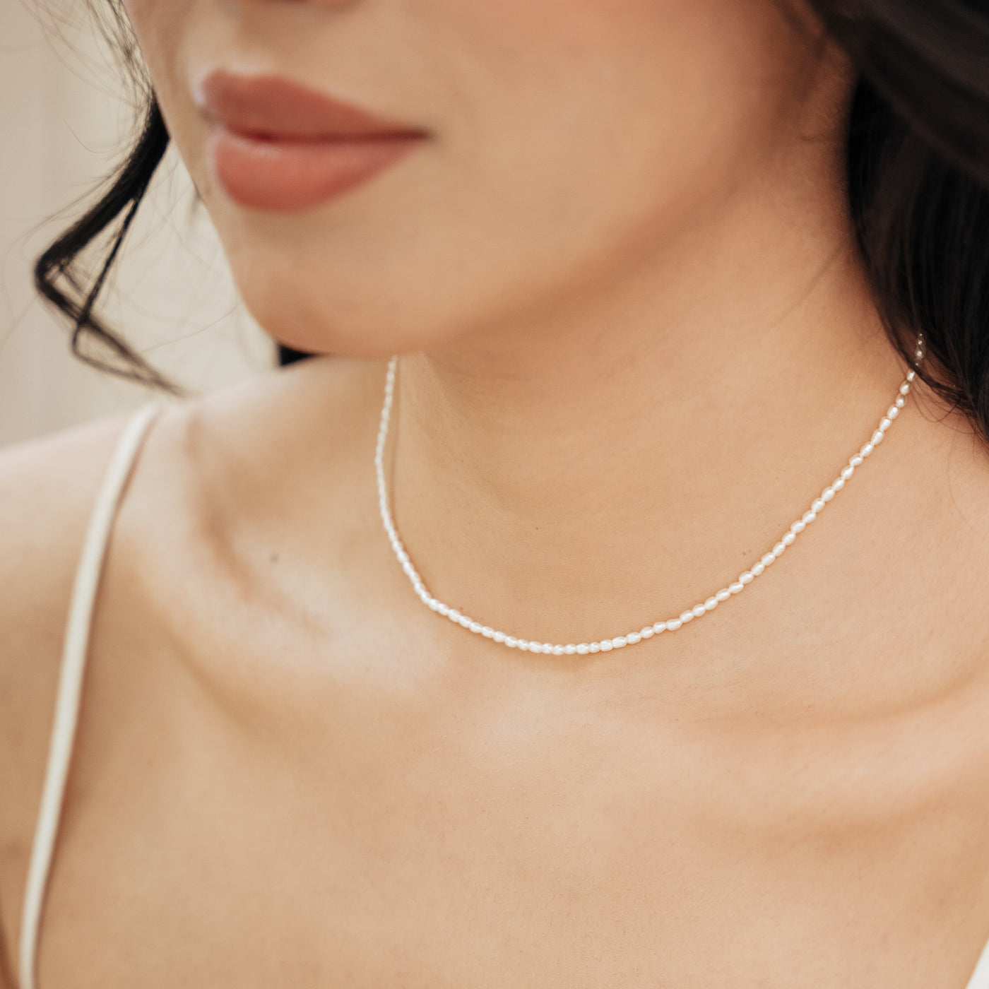 Close-up of a woman’s chest wearing the Dainty Pearl Strand Necklace.