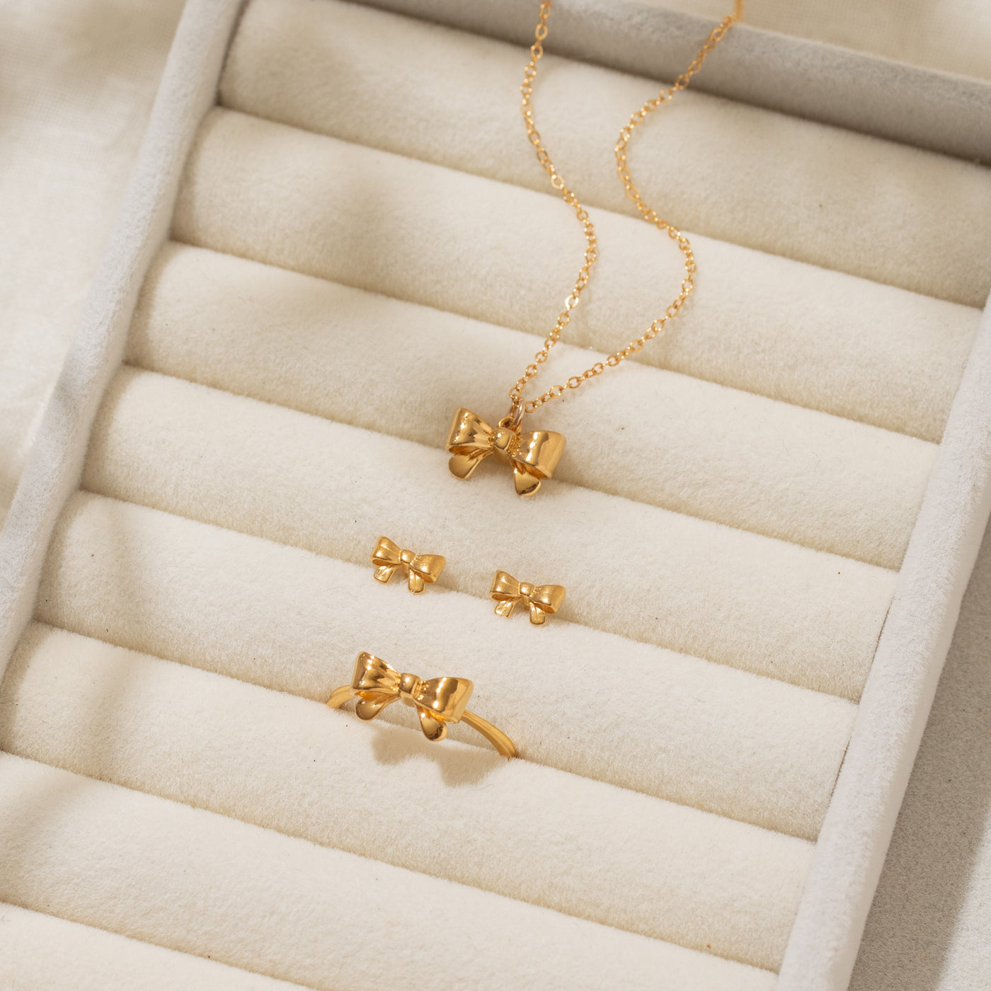 Close-up of a jewelry organizer displaying the Ribbon Bow Necklace, Ribbon Bow Stud Earrings, and Ribbon Bow Ring. 