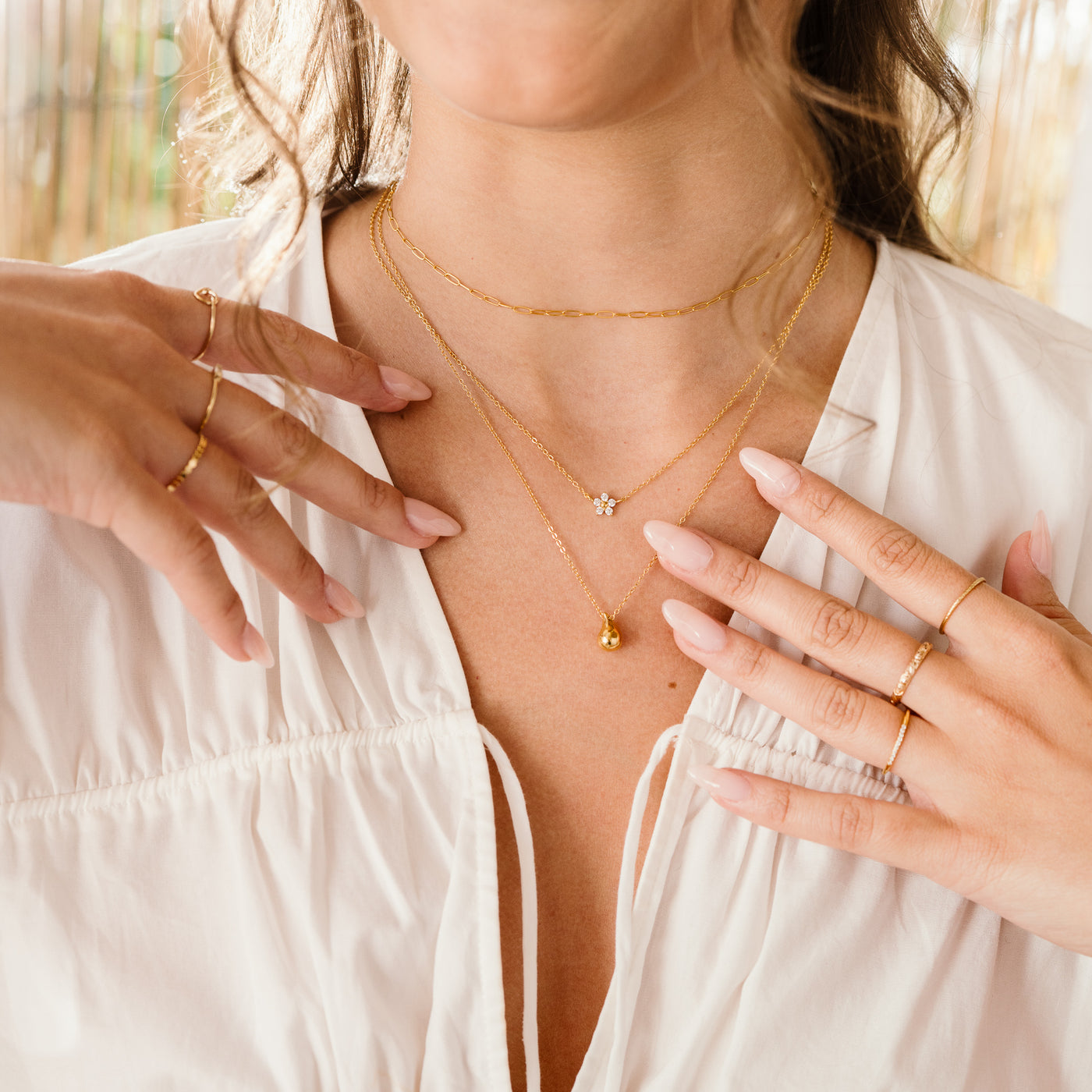 Small Large Teardrop Pendant Necklace Woman's neck closeup. She's wearing a white shirt and jewelry, including 3 necklaces: dainty paperclip, flower CZ, and dainty teardrop necklace and 3 rings on each hand. Left hand: heart knot ring, dainty baguette, and flat band and on right: pavé CZ ring, rose ring, and simple stackign ring.
