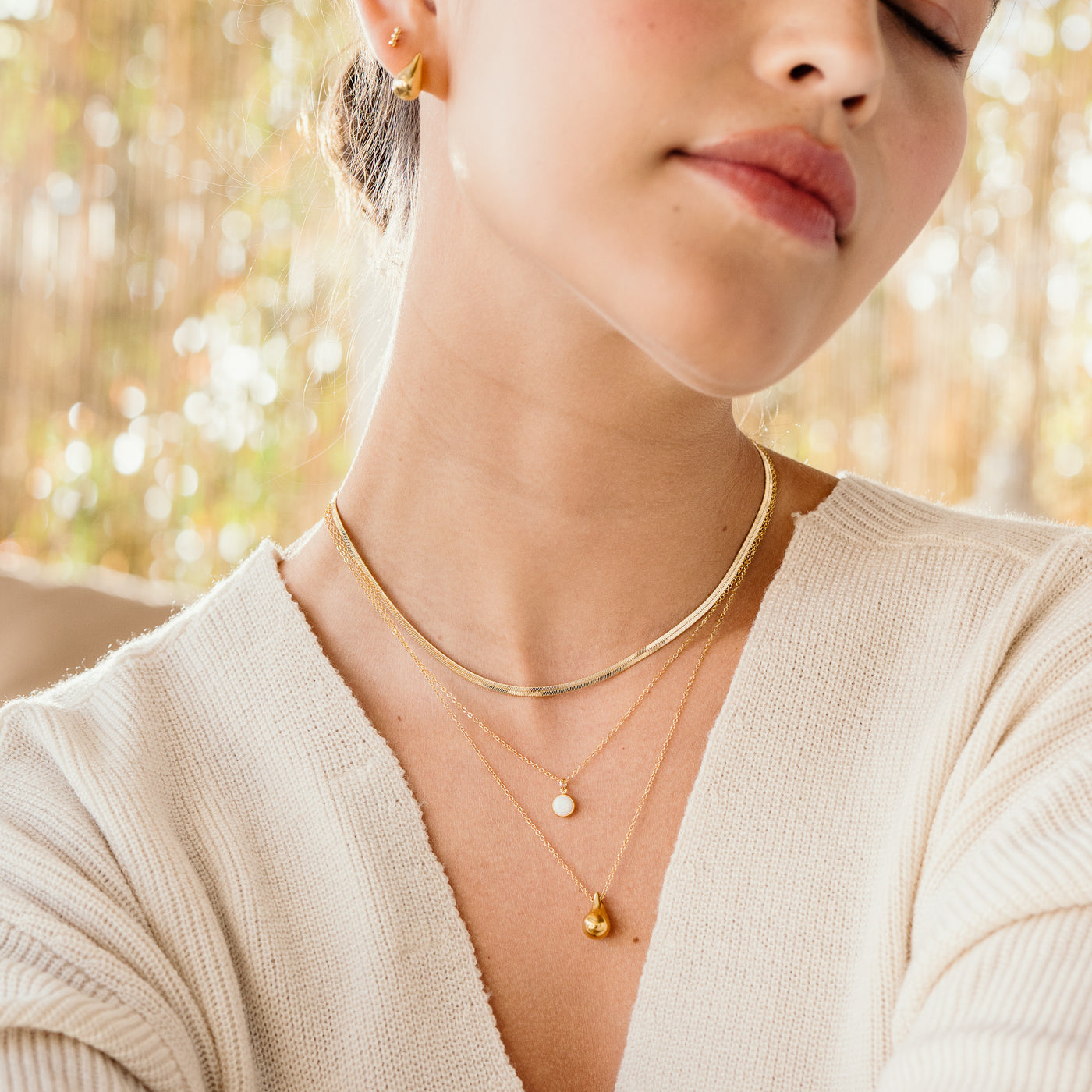 Small Large Teardrop Pendant Necklace Woman from the chest up. looking to the side with her eyes closed. She's wearing gold herringbone necklace, opal necklace, teardrop necklace, teardrop stud earrings, and bead bar studs.