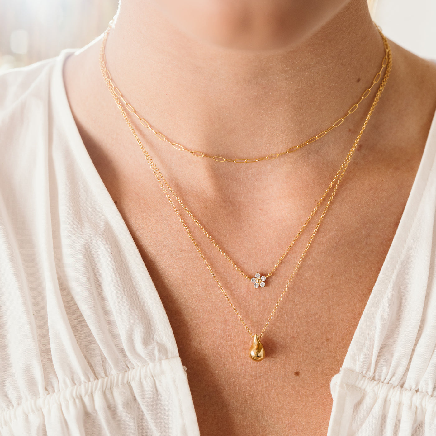 Small Large Teardrop Pendant Necklace woman's neck closeup. She's wearing 3 necklaces, from top to bottom: dainty paperclip chain, flower CZ, and dainty teardrop necklace.