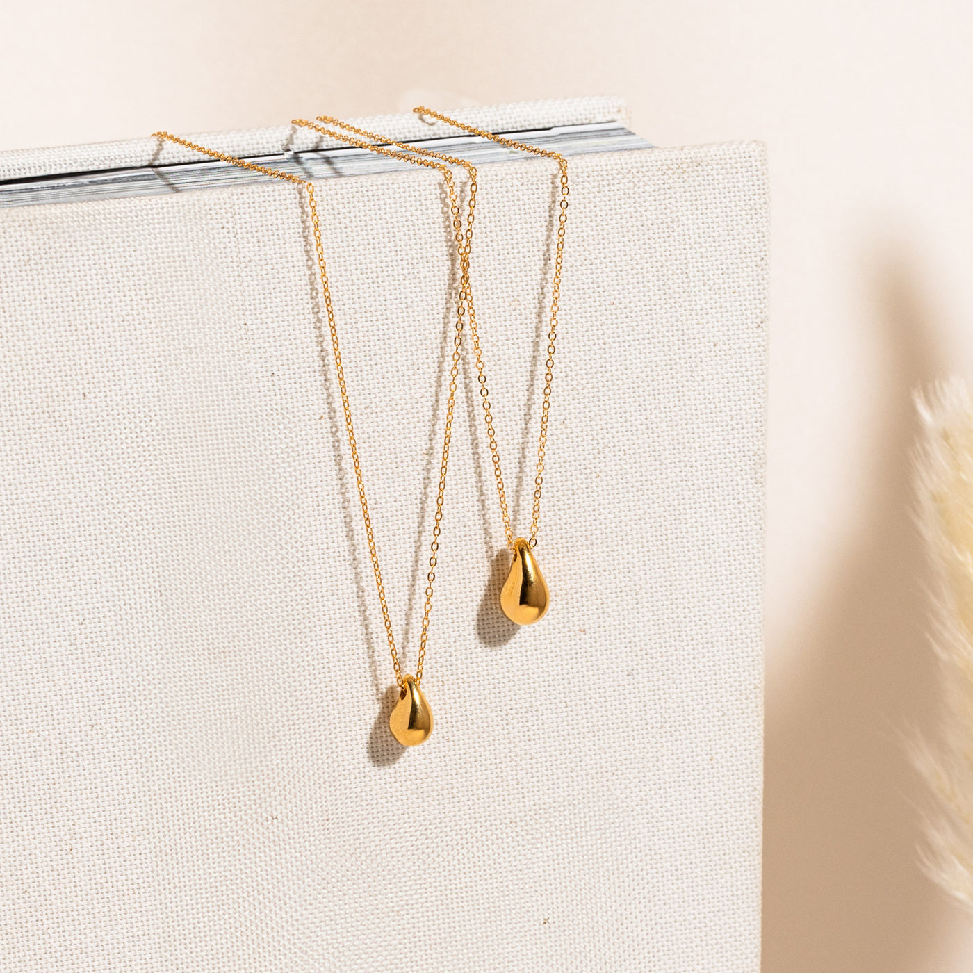 Small Large Teardrop Pendant Necklace. Dainty teardrop and teardrop necklace displayed vertically on a textured white backdrop.