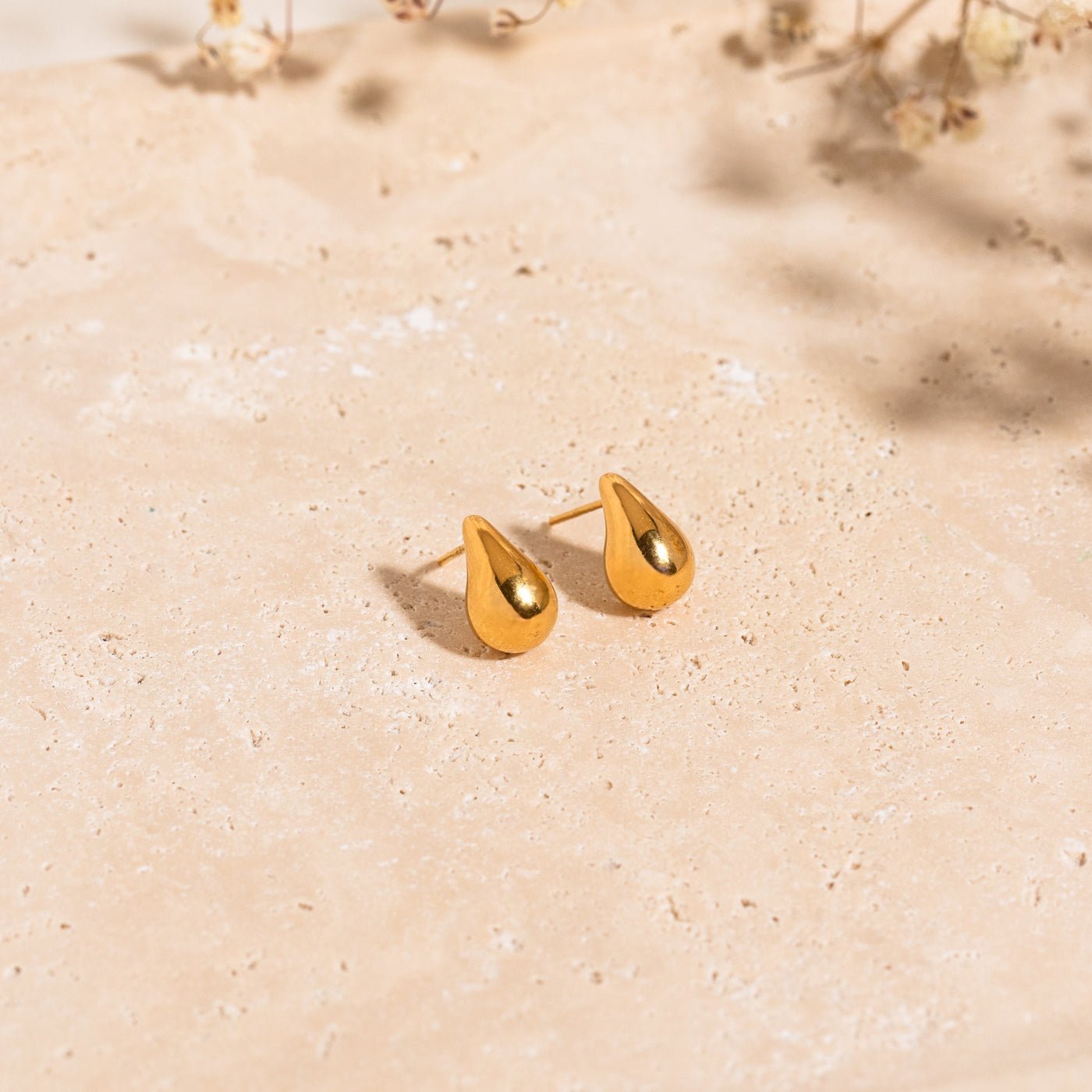 Small Large Teardrop Stud Earrings Dainty teardrop stud earrings lying on a stone surface