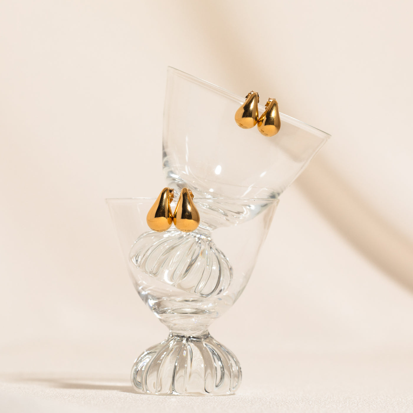 Small Large Teardrop Stud Earrings teardrop stud earrings, one smaller pair and one larger pair, resting on the edge of stacked glass cups in balance.