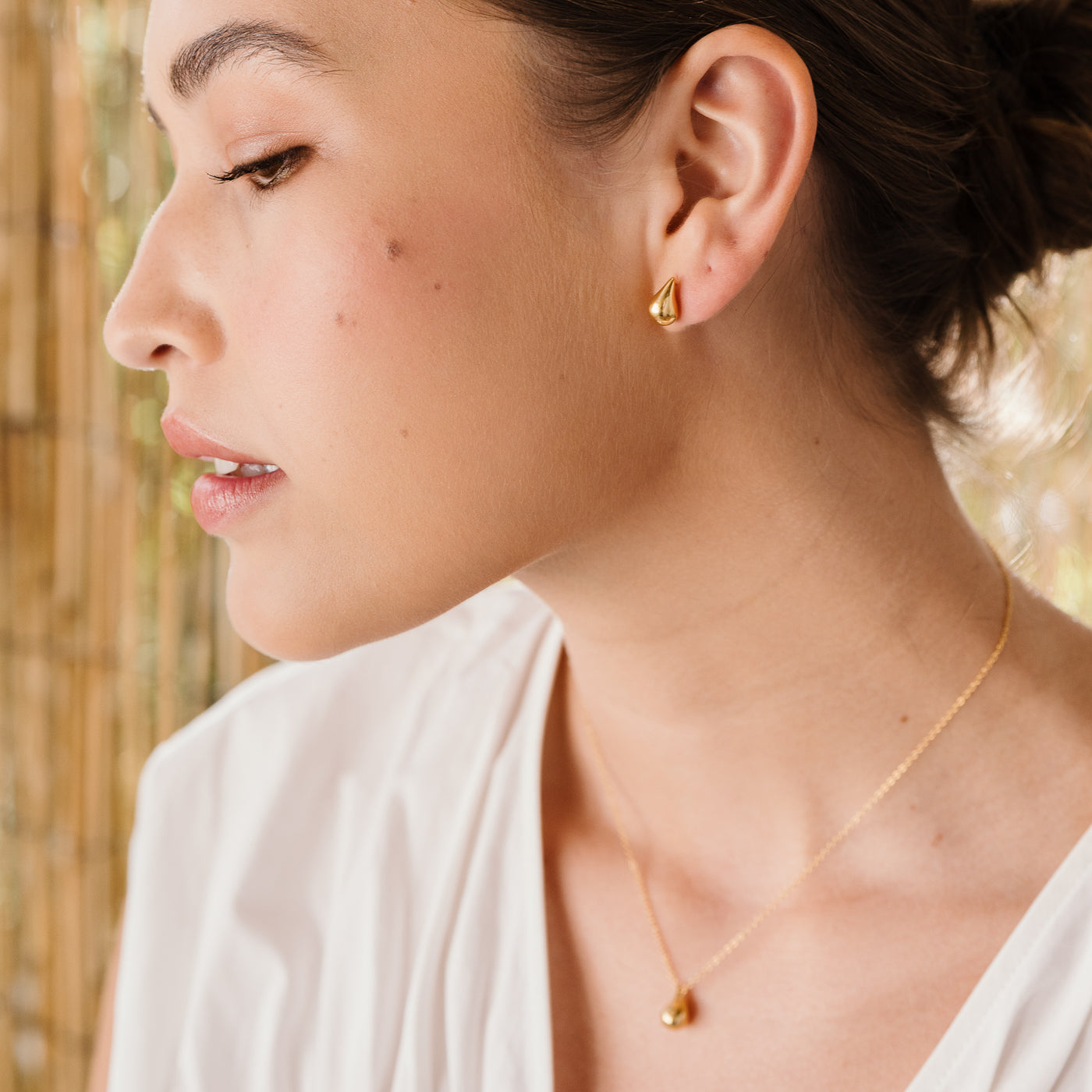 Small Teardrop Stud Earrings Woman looking to the left, wearing dainty teardrop stud earrings and a teardrop pendant necklace.