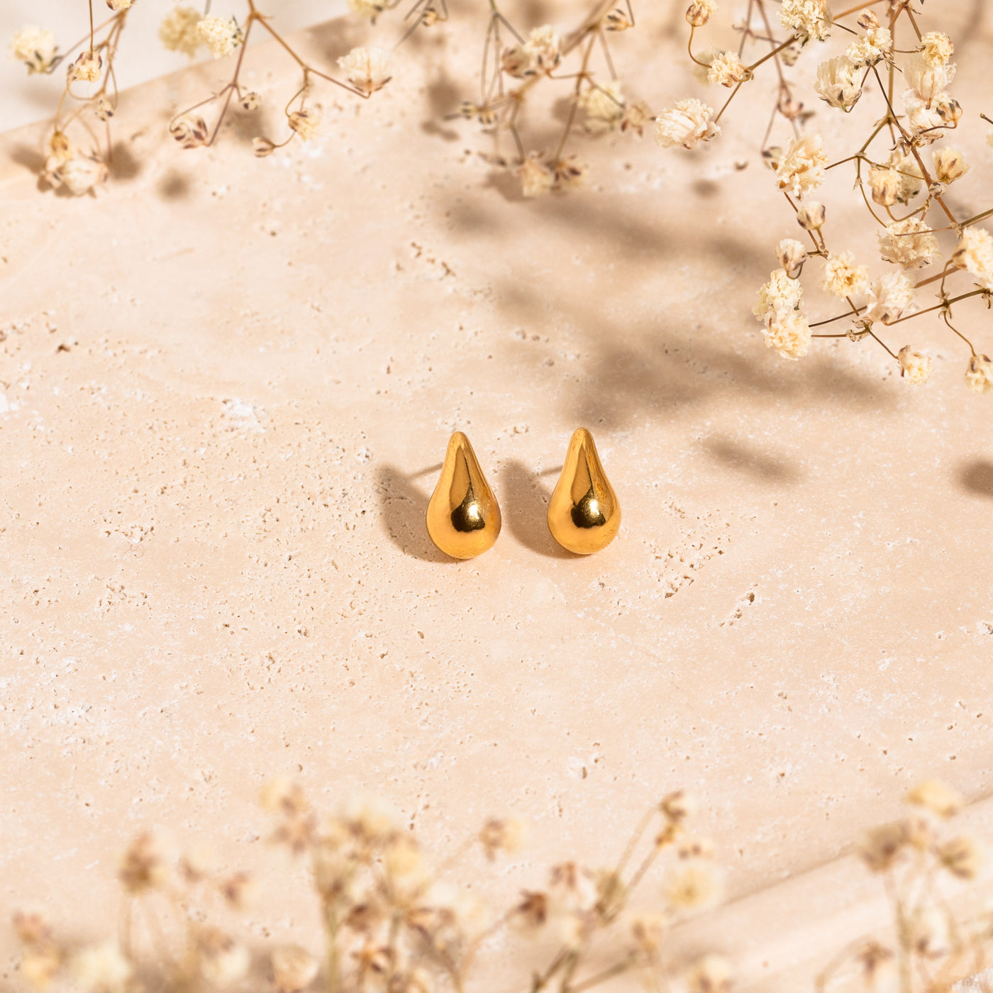 Small Large Teardrop Stud Earrings Dainty teardrop stud earrings lying on a stone surface surrounded by baby’s breath flowers.