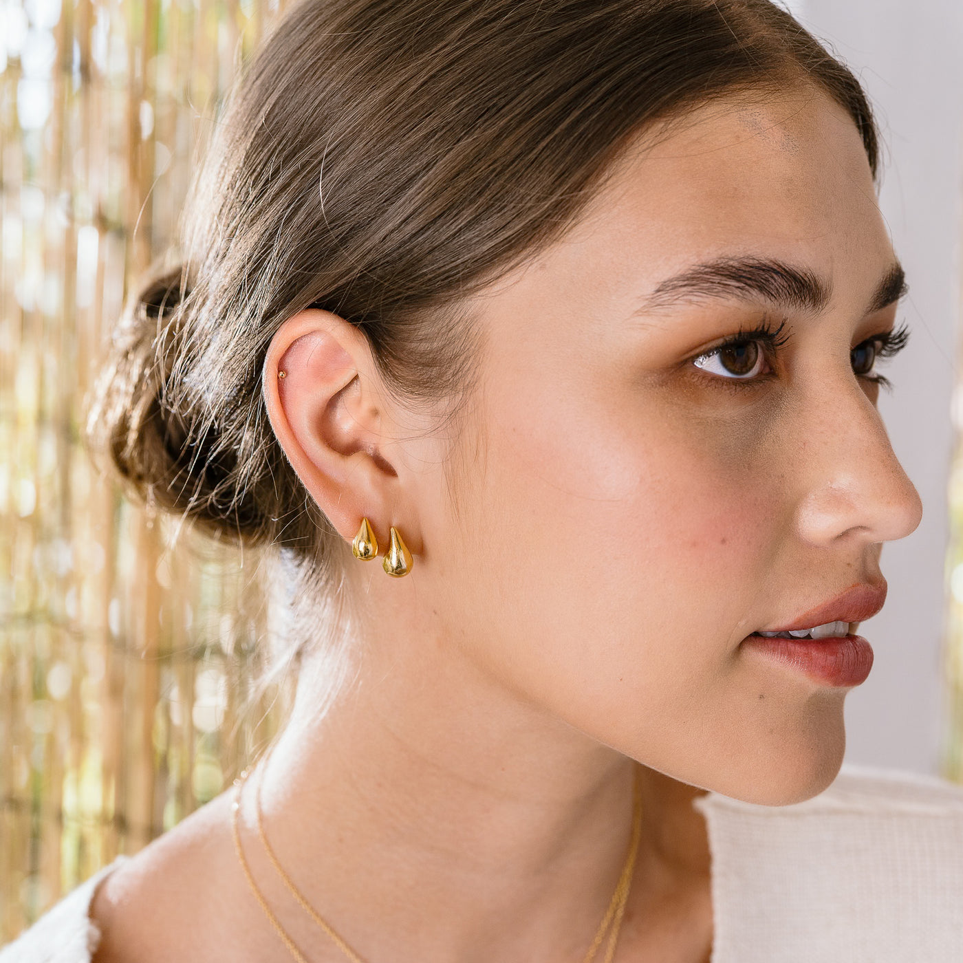 Small Large Teardrop Stud Earrings. Woman's face. She's looking to the side and wearing teardrop stud earrings, and dainty teardrop stud earrings on her right ear