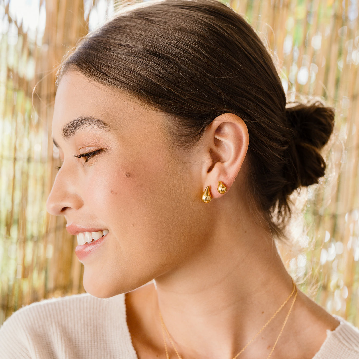 Small Large Teardrop Stud Earrings. Woman in profile, smiling, wearing two teardrop stud earrings—a larger one and a smaller one—on her left ear.
