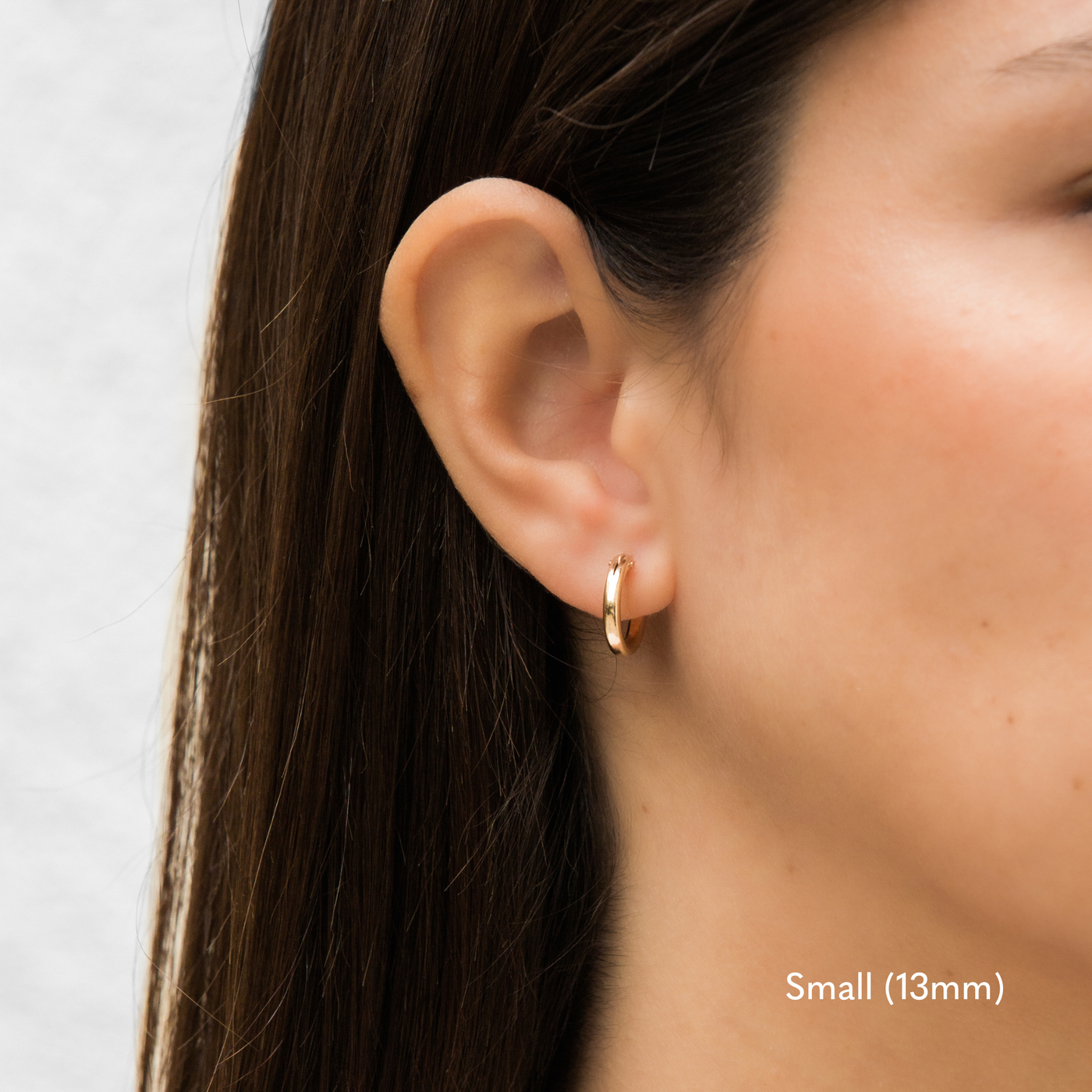 Woman wearing a single small 13mm gold Everyday Hoop Earring on one ear. The photo is taken from the side, showing her earring, and hair pulled back,.

Small (13mm) 