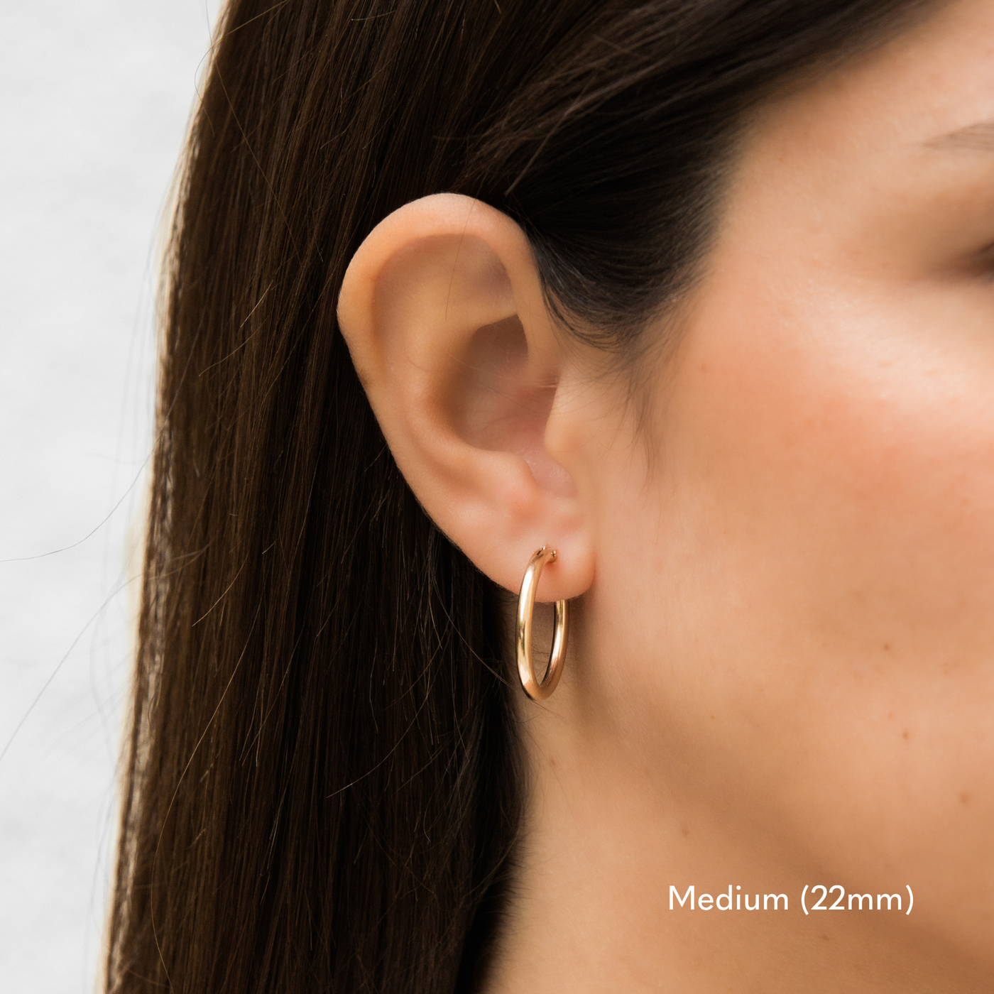 Woman wearing a single medium 22mm gold Everyday Hoop Earring on one ear. The photo is taken from the side, showing her earring, and hair pulled back.

Medium (22mm)