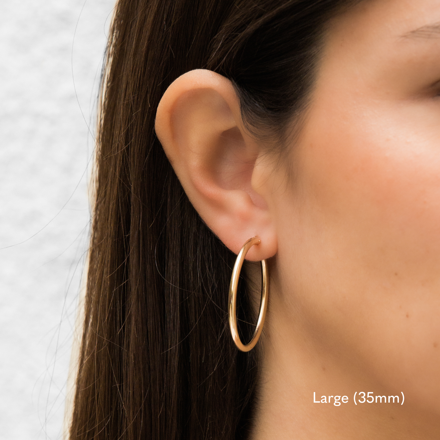 Woman wearing a single large 35mm gold Everyday Hoop Earring on one ear. The photo is taken from the side, showing her earring, and hair pulled back.

Large (35mm)