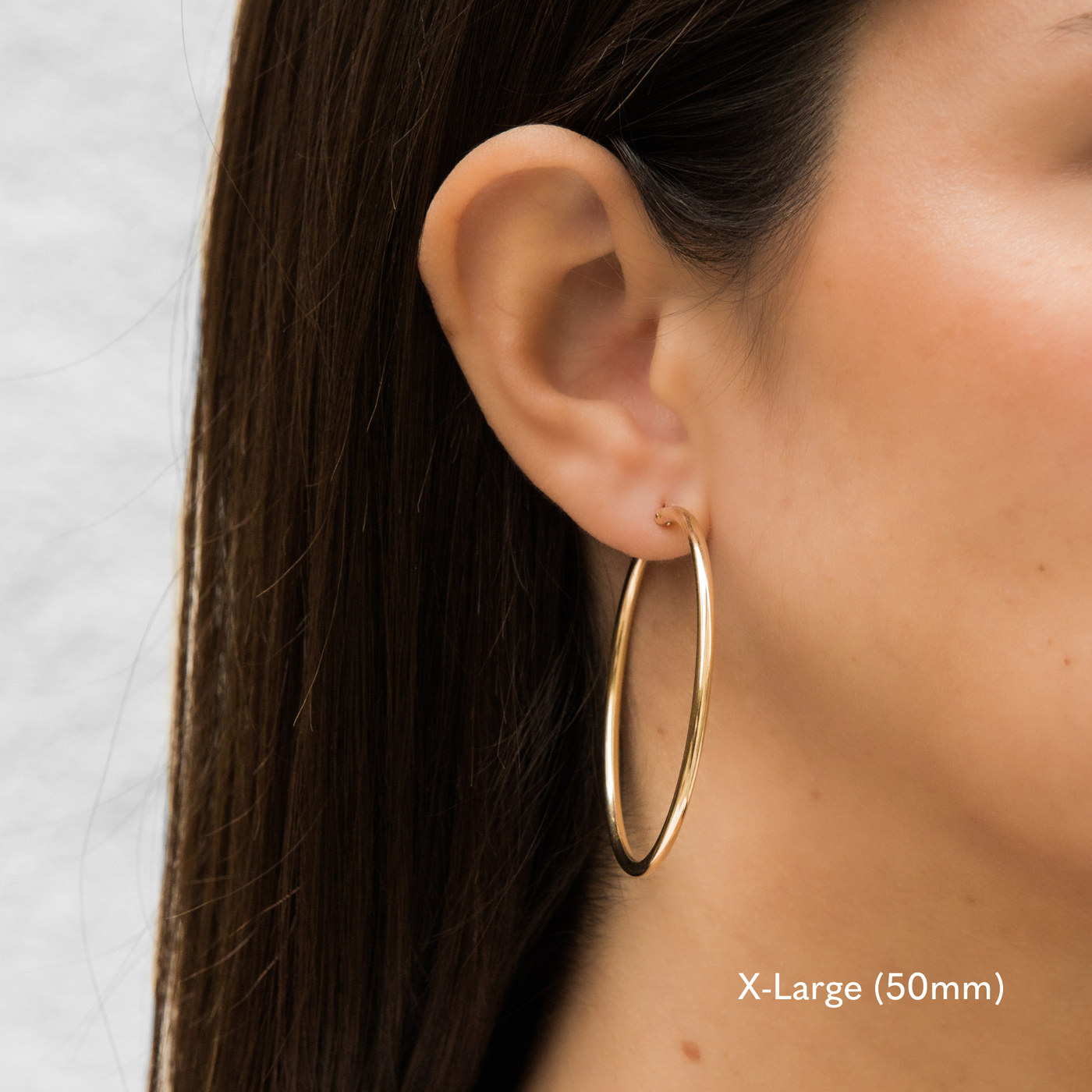 Woman wearing a single extra large 50mm gold Everyday Hoop Earring on one ear. The photo is taken from the side, showing her earring, and hair pulled back.

X-Large (50mm), Everyday Hoop Earrings by Simple & Dainty Jewelry