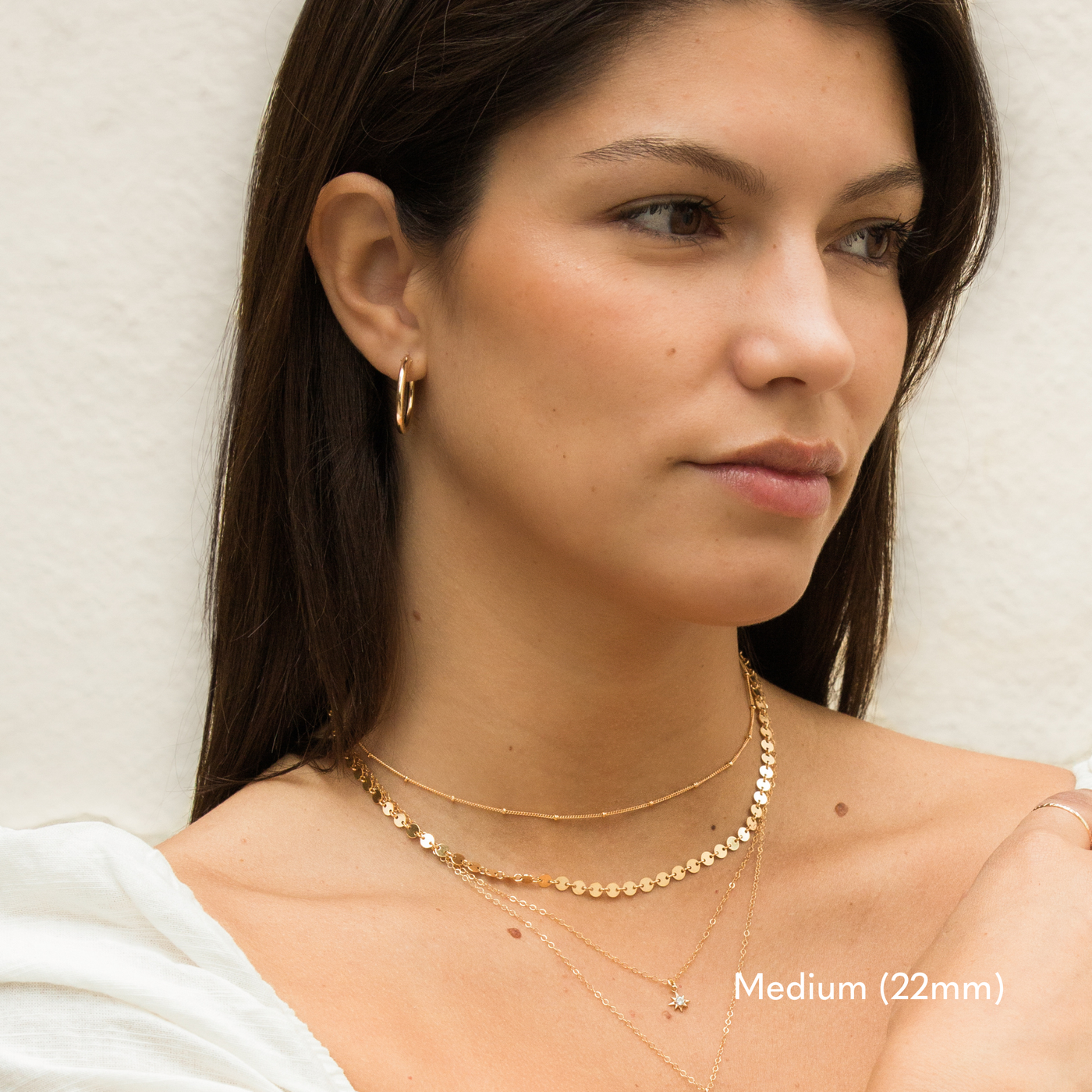 Side view of a woman’s face showing a medium 22mm gold hoop earring on her right ear. She has long dark hair tucked behind her ear, with a soft beige background.

Small (13mm) Medium (22mm) Large (35mm) Everyday Hoop Earrings by Simple & Dainty Jewelry