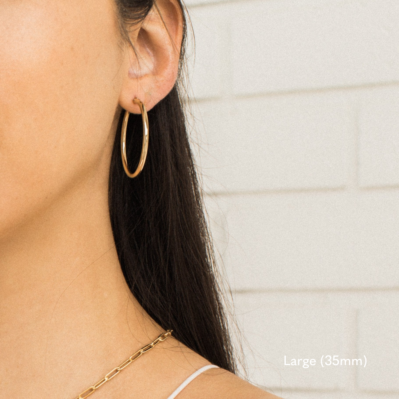 Woman wearing a single large 35mm gold Everyday Hoop Earring on one ear. The photo is taken from the side, showing her earring, hair pulled back, and a small portion of her shoulder.

Small (13mm) Medium (22mm) Large (35mm) Everyday Hoop Earrings by Simple & Dainty Jewelry