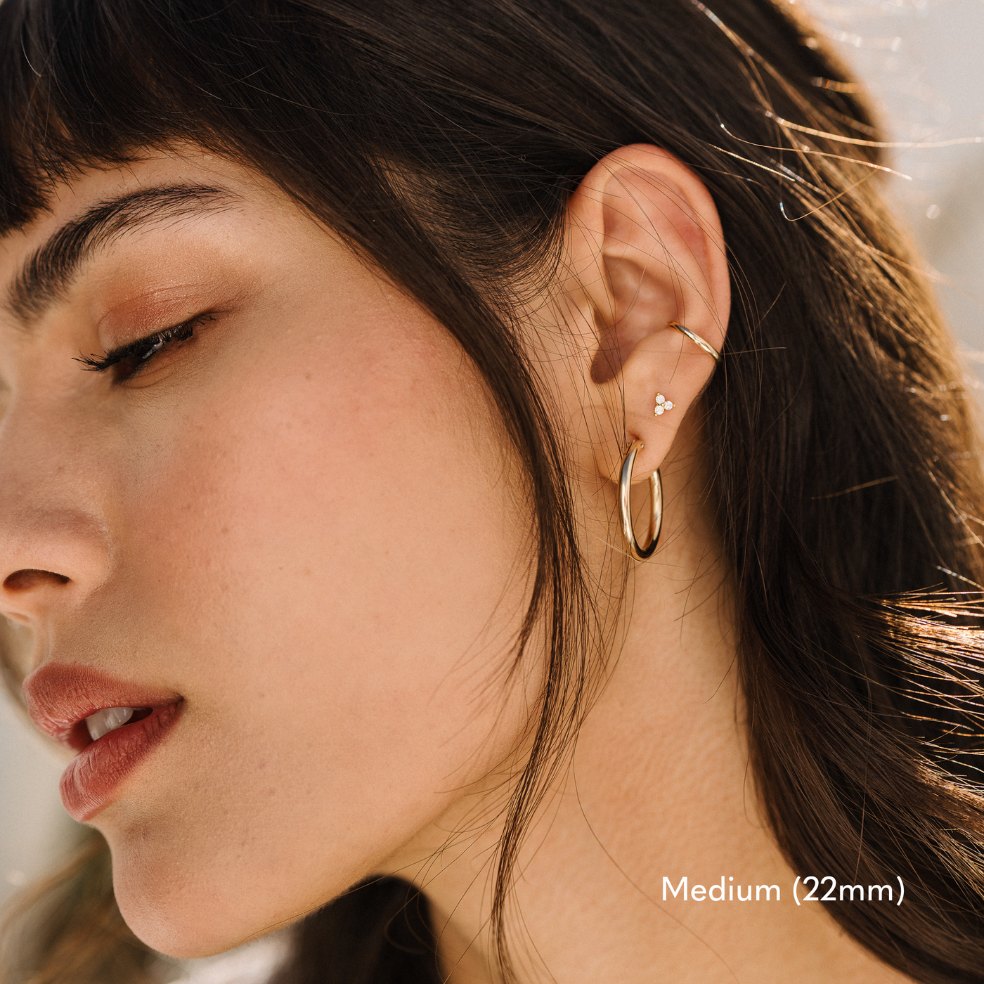 Woman with sleek black hair, wearing a gold 22mm medium Everyday Hoop earring, layered with a delicate stud and a minimalist ear cuff for a chic stacked look.

Small (13mm) Medium (22mm) Large (35mm) Everyday Hoop Earrings by Simple & Dainty Jewelry