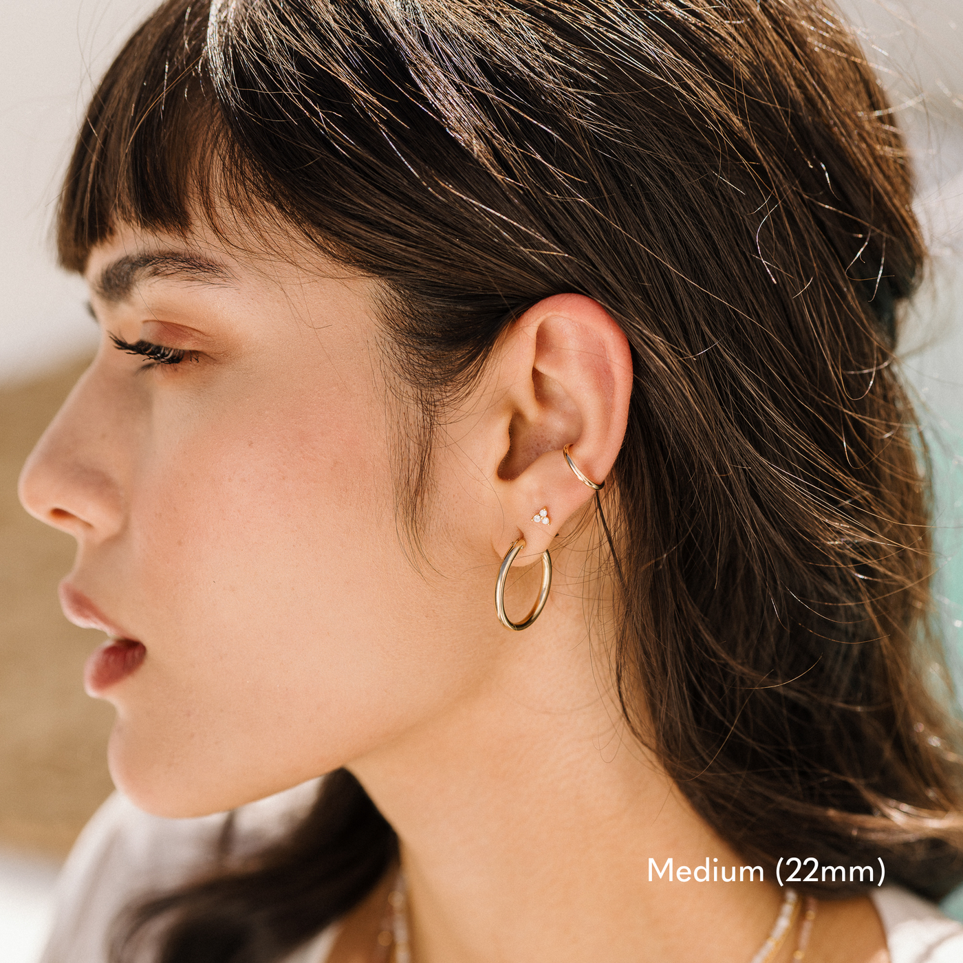 Woman with sleek black hair, wearing a gold 22mm medium Everyday Hoop earring, layered with a delicate stud and a minimalist ear cuff for a chic stacked look.

Small (13mm) Medium (22mm) Large (35mm) Everyday Hoop Earrings by Simple & Dainty Jewelry