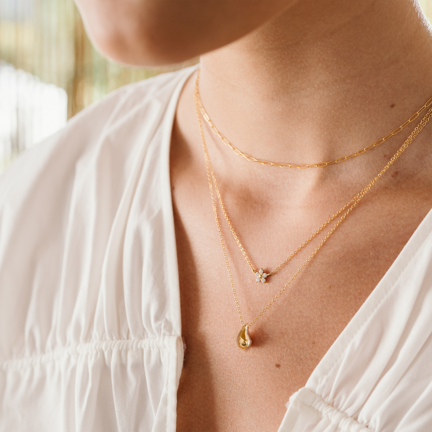 Close-up of a woman wearing two gold necklaces with floral and teardrop pendants.