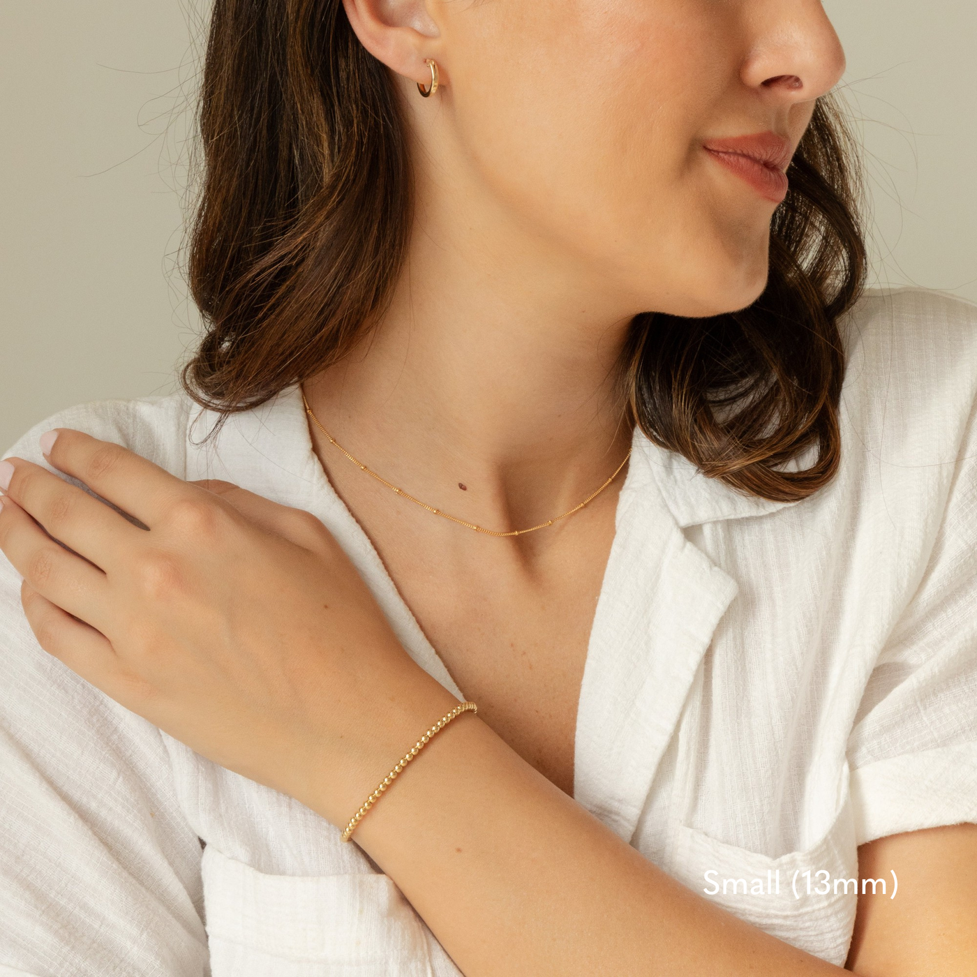 Woman in a crisp white top wearing a small 13mm gold Everyday Hoop earring that gently catches the light, paired with a delicate, dainty gold chain draping around her neck and a simple, colorful beaded bracelet resting on her wrist.

Small (13mm) Medium (22mm) Large (35mm) Everyday Hoop Earrings by Simple & Dainty Jewelry